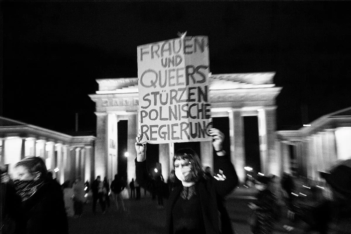 eine Person hält ein Schild mit der Aufschrift Frauen und Queers stürzen polnische Regierung, im Hintergrund das Brandenburger Tor