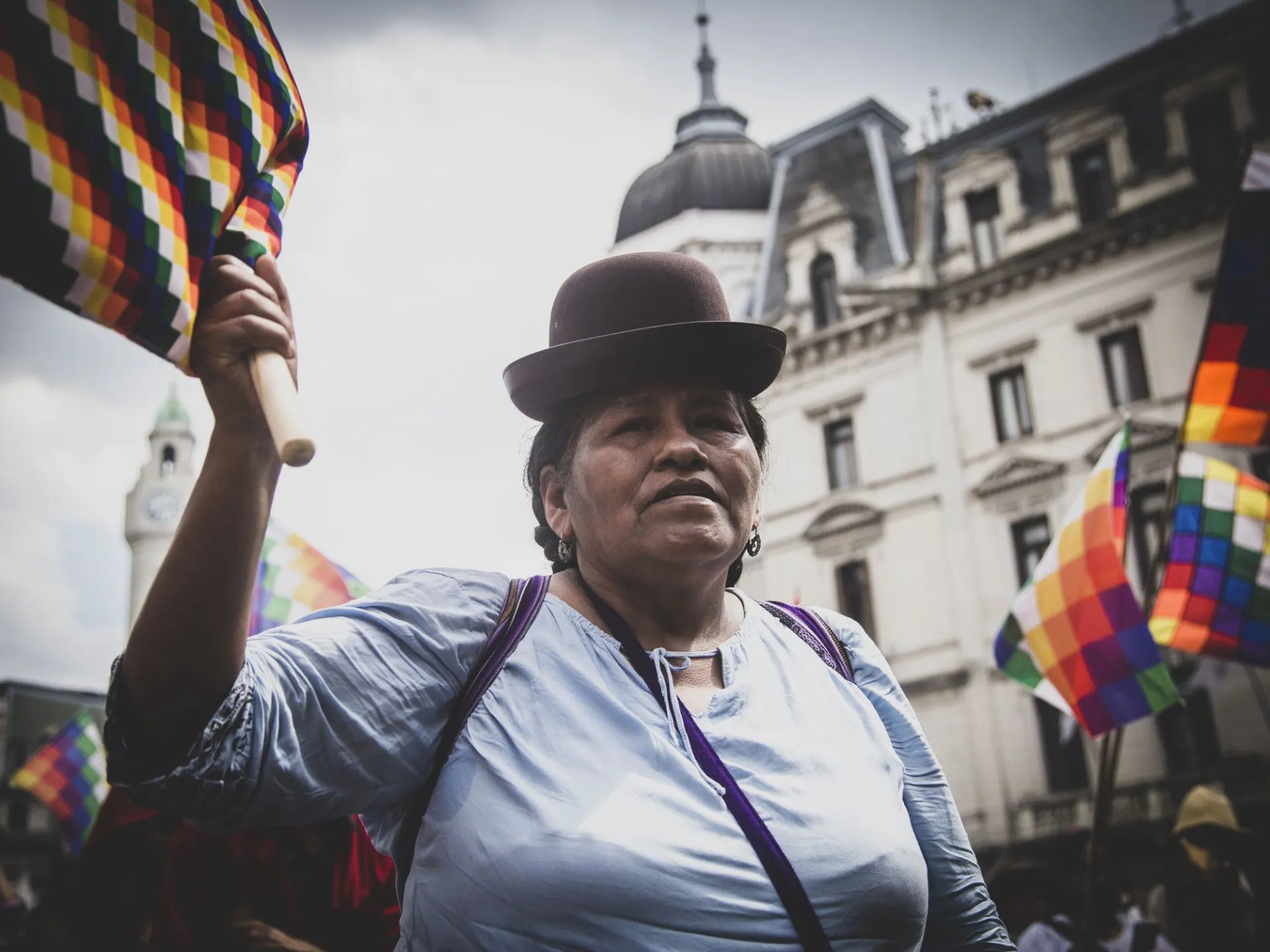 Eine indigene Frau in Bolivien schwenkt die Wiphala, die Fahne der Farben, die alle Völker Boliviens repräsentiert.