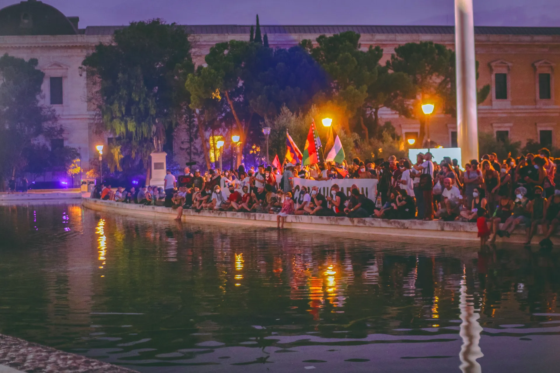 viele Menschen mit Bannern und Fahnen sitzen und stehen an einem Kanal