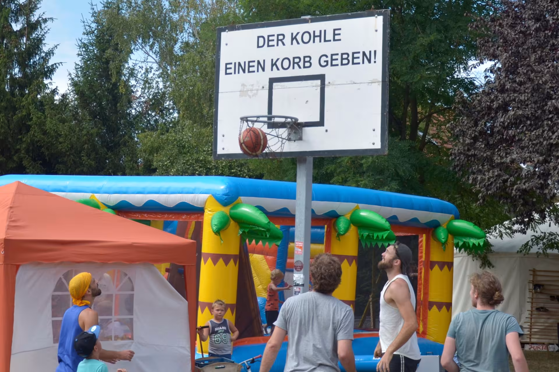 Menschen spielen Basketball, auf dem Korb steht "Der Kohle einen Korb geben"