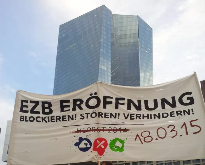 Hochhaus (EZB) im Hintergrund davor Banner: EZB Eröffnung Blockieren! Stören! Verhindern!