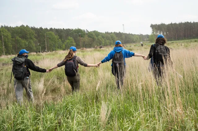 Vier Menschen mit blauen Kappen laufen sich an den hände haltend über eine Wiese. 
