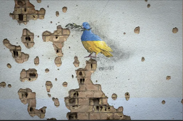 abblätterndes Wandbild einer Friedenstaube in ukrainischen Nationalfarben auf einer Backsteinwand