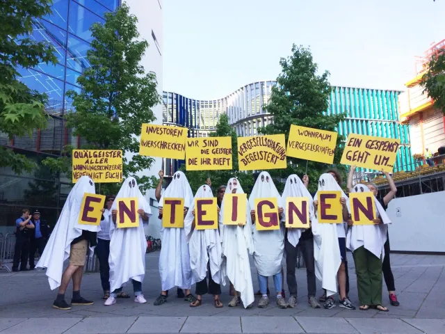 als Geister verkleidete Demonstrant*innen halten Schilder mit den Buchstaben enteignen hoch sowie andere Schilder mit den Aufschriften Investoren (v)erschrecken, Wir sind die Geister die ihr rieft oder Vergesellschaftung begeistert