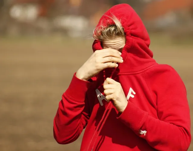 eine Person zieht die Kapuze ihres roten Kapuzenpullis fest gegen einen starken Wind