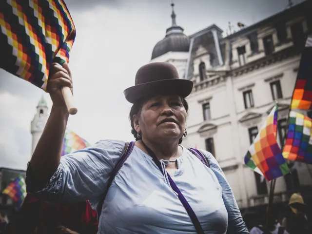 Eine indigene Frau in Bolivien schwenkt die Wiphala, die Fahne der Farben, die alle Völker Boliviens repräsentiert.