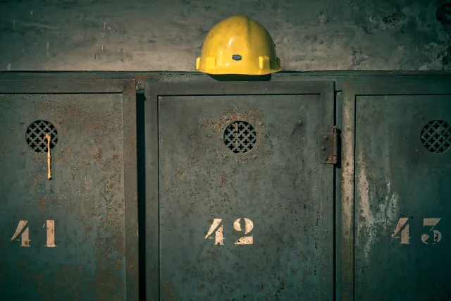 drei Metallspinde stehen nebeneinander, auf dem mittleren liegt ein gelber Helm