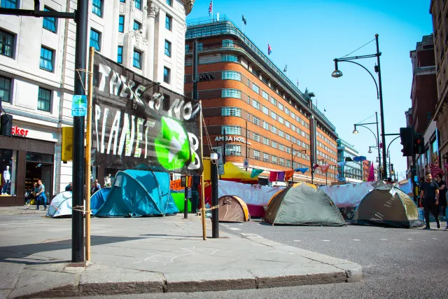 ein Camp mit Zelten an einer Straßenkreuzung, im Vordergrund ein Banner mit der Aufschrift There is no planet B