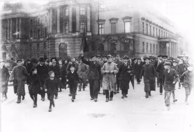 Szene der Novemberrevolution, viele Menschen laufen Richtung Kamera, vorneweg einer mit erhobener Fahne