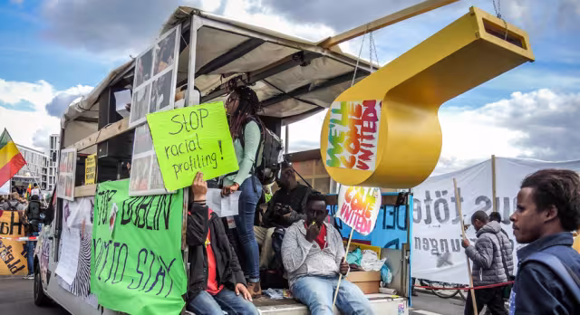 auf einem Lautsprecherwagen halten Menschen Schilder mit der Aufschrift "stop racial profiling!" und "We'll come united"