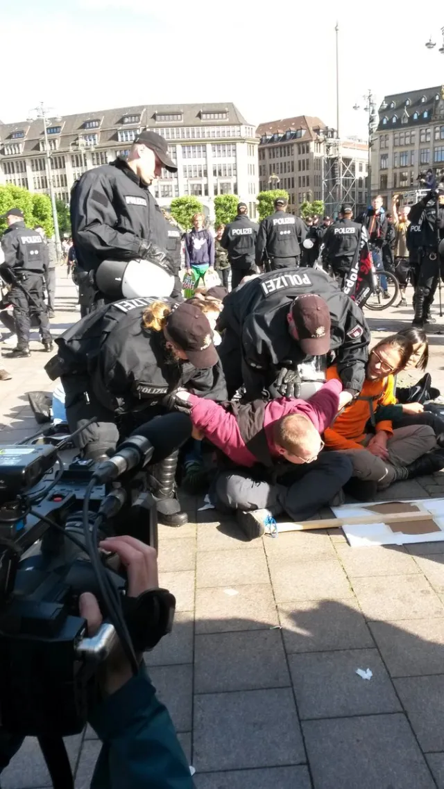 Sitzblockade. Polizisten greifen sitzenden Aktivisti an den Armen.
